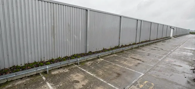 Moss and debris collected along the gutter line of a large clad commercial building